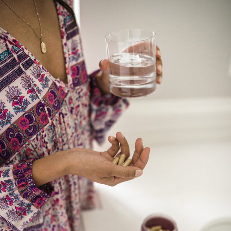 photo of a girl holding 3 capsules of WeNatal prenatal supplement in her right hand while carrying a glass of water on her left hand