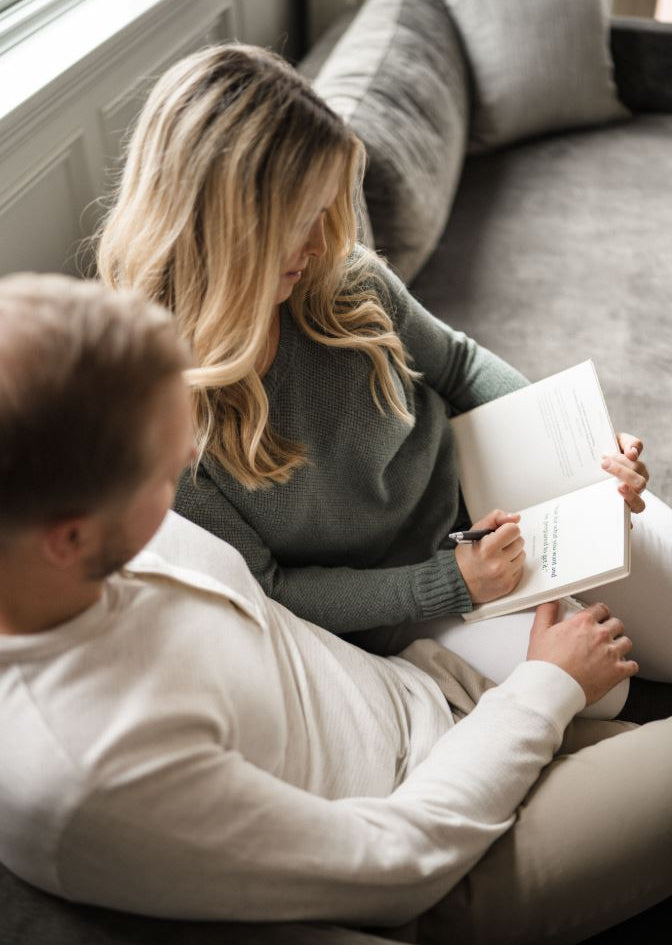 man and woman sitting on couch journaling together - fertility cliff - WeNatal prenatal
