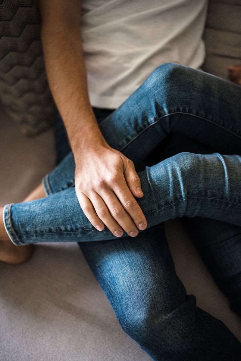 man sitting on couch with woman’s legs overlapping his and his hand on top - WeNatal 