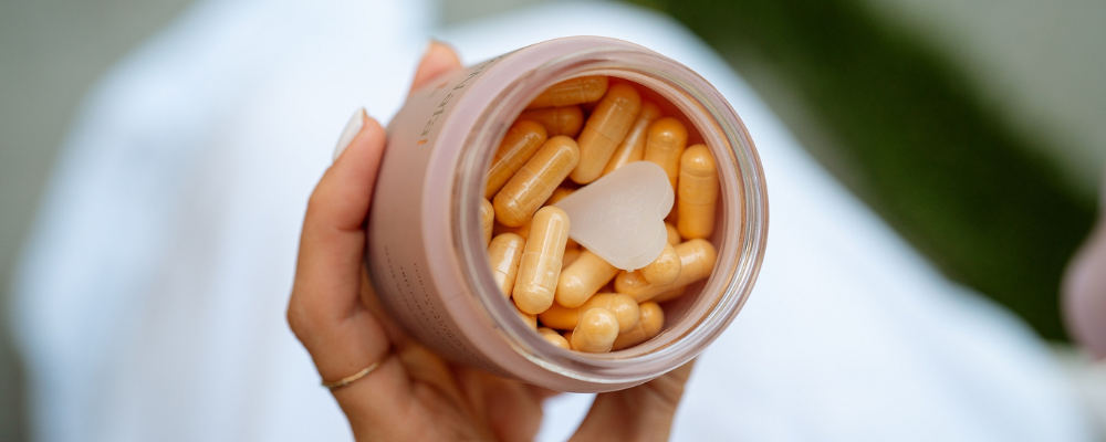 a hand holding WeNatal For Her prenatal supplements capsules inside its jar with the heart-shaped mint scent above the capsules