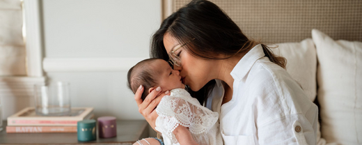 mother kissing newborn baby at home on bed - building your village before baby WeNatal