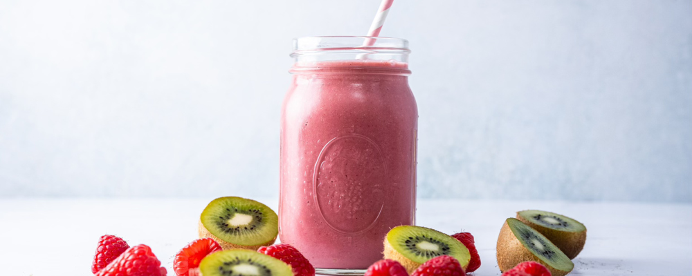 A vibrant pink smoothie in a glass jar with a striped straw, surrounded by fresh kiwi slices and raspberries, highlighting a refreshing, nutrient-rich drink for health and wellness