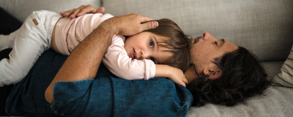 Father resting on a couch holding his young child, showcasing warmth and emotional bonding, highlighting nurturing parenthood and family well-being