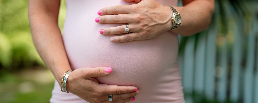 A pregnant woman holds her belly, showcasing her wedding ring and stylish accessories, reflecting WeNatal's focus on prenatal wellness and lifestyle