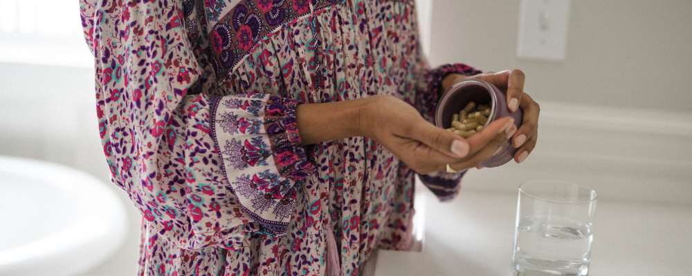 Woman pouring prenatal vitamins into her hand from a bottle, preparing to take them with water. She is focused on her daily health routine, emphasizing wellness and prenatal care. -WeNatal
