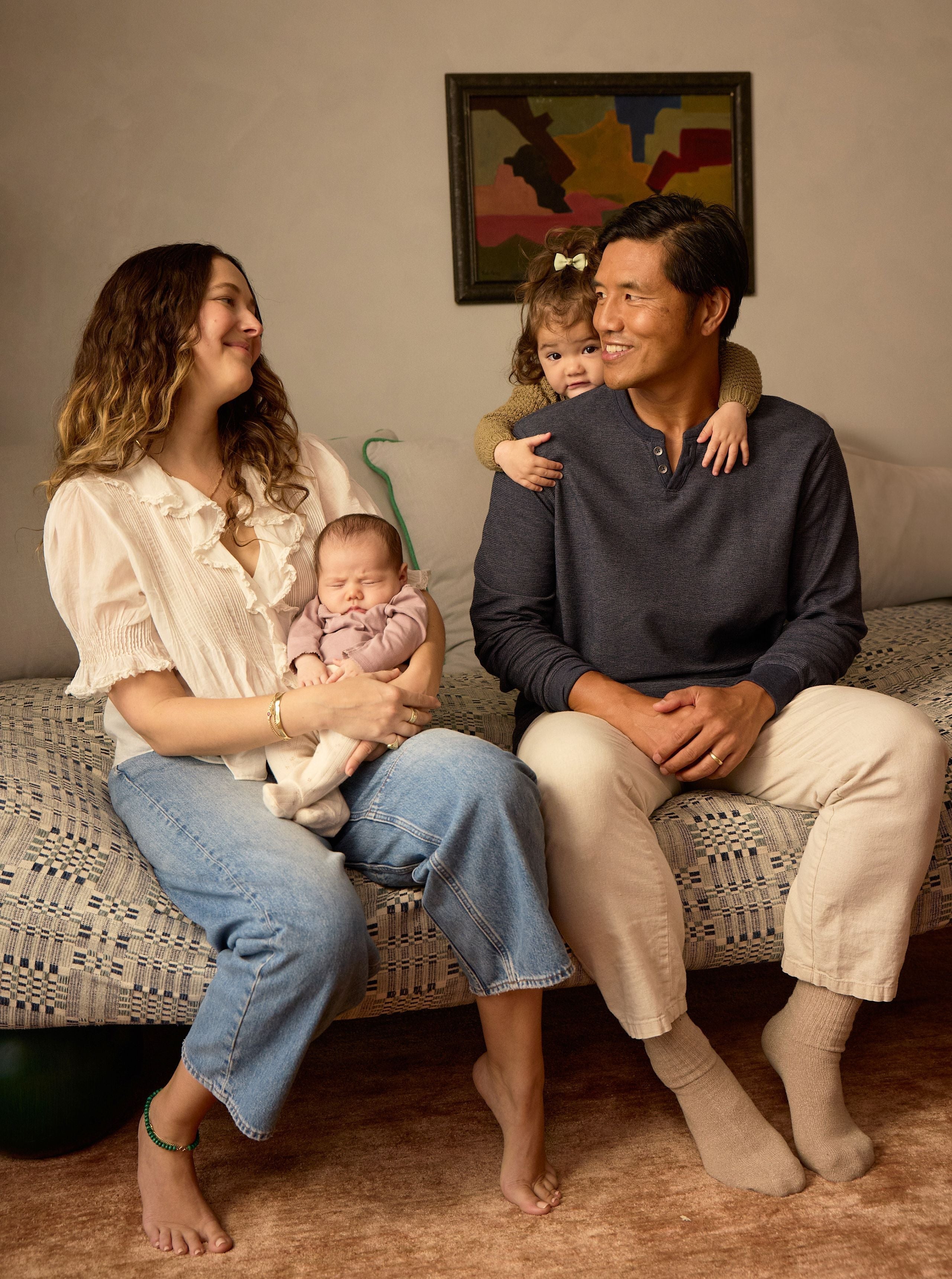 woman holding newborn on bed with husband and daughter sitting next to her smiling at each other - WeNatal prenatal for postpartum - c section recovery