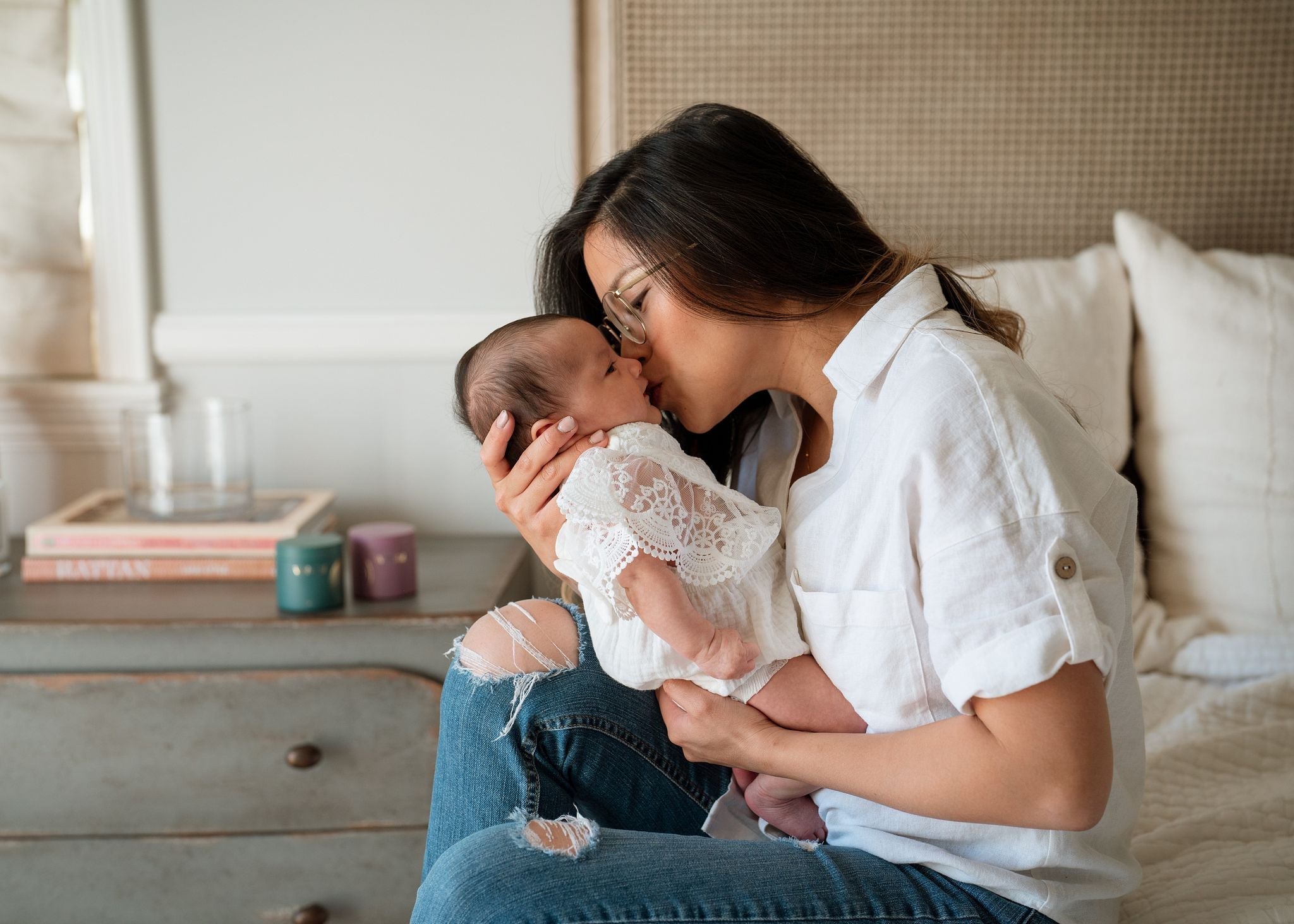 mother holding baby on bed giving it a kiss - postpartum - fourth trimester - WeNatal prenatals