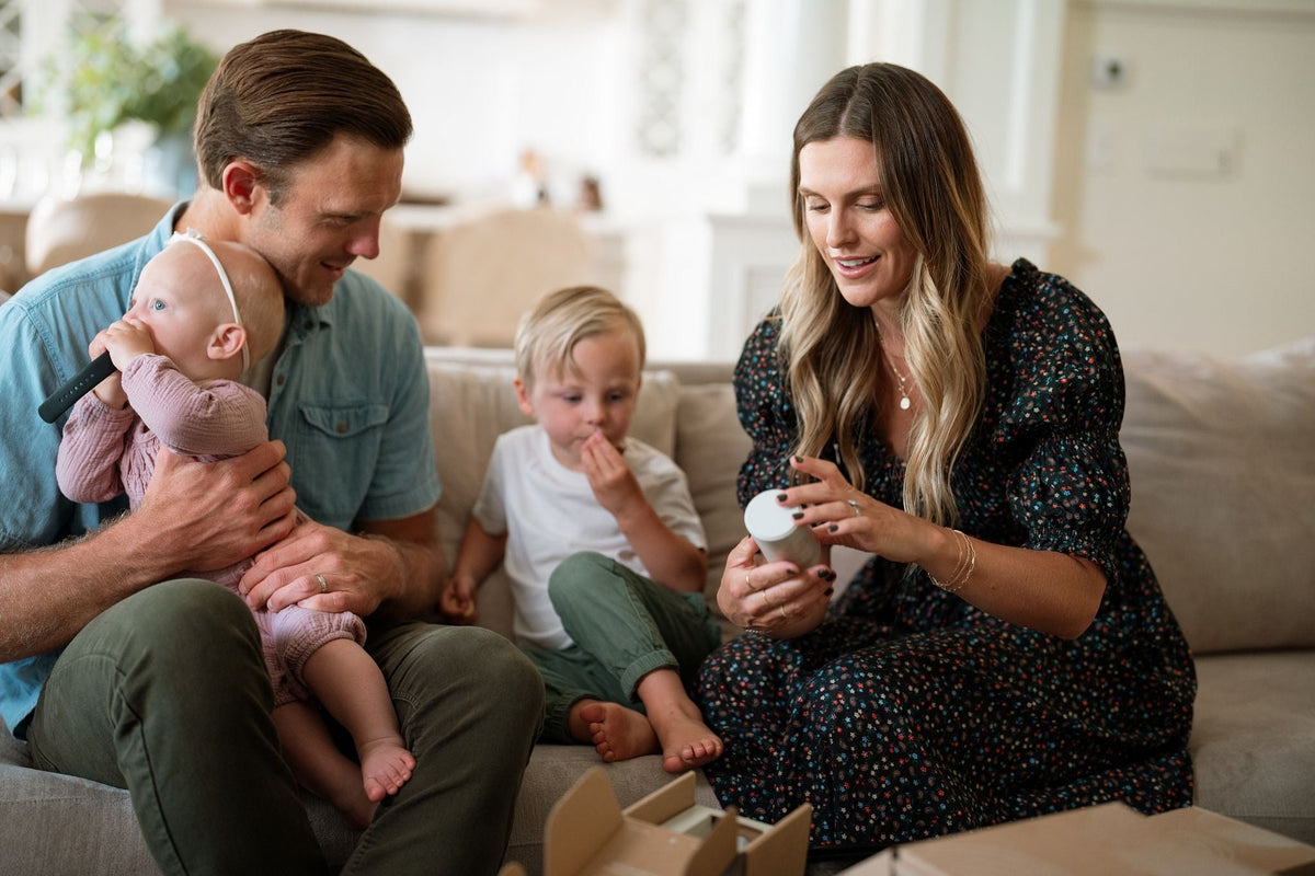 man with baby on lap next to woman with toddler next to her looking at a jar of supplements - WeNatal prenatal