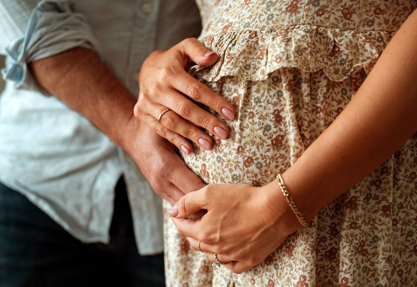 close up image of woman holding pregnant stomach with husband’s hand over stomach - WeNatal prenatal - pregnancy after 35