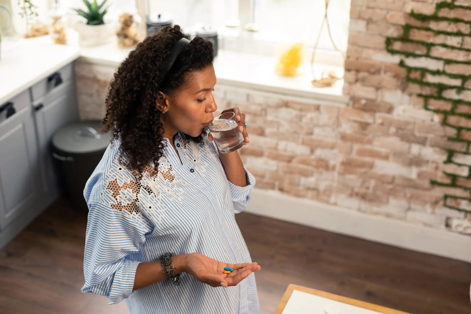 A woman drinks water and holds a pill, reflecting WeNatal's focus on prenatal vitamin supplements.