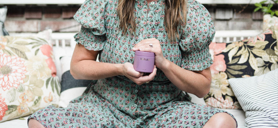 Woman sitting outside holding a glass container of prenatal vitamins - WeNatal for Her 