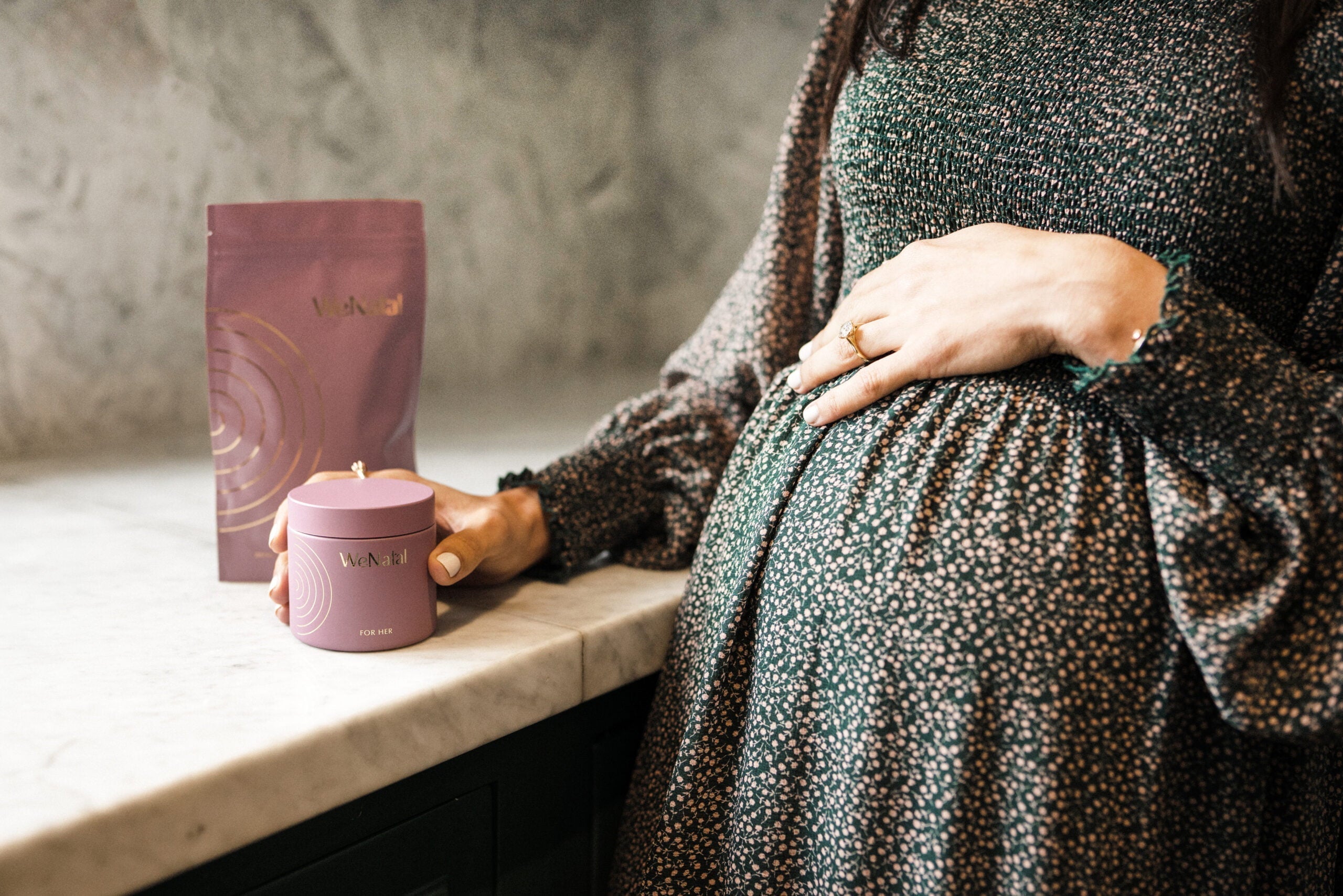 Pregnant woman with hand on top of stomach holding supplement jar with supplement pouch next to her - WeNatal prenatals