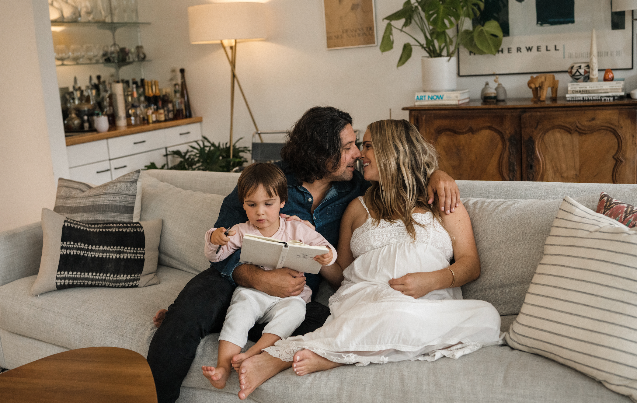 Couple sitting on couch with child reading a book and mother holding pregnant belly - mitochondrial health for fertility - WeNatal