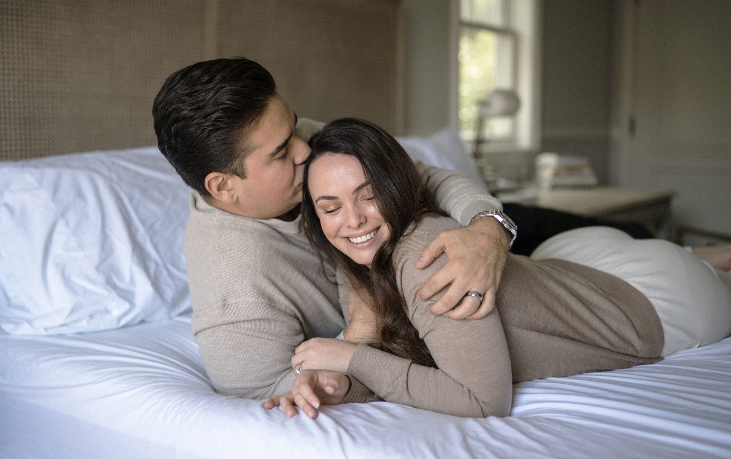 couple laying on bed with husband holding wife and kissing her on the head - WeNatal 
