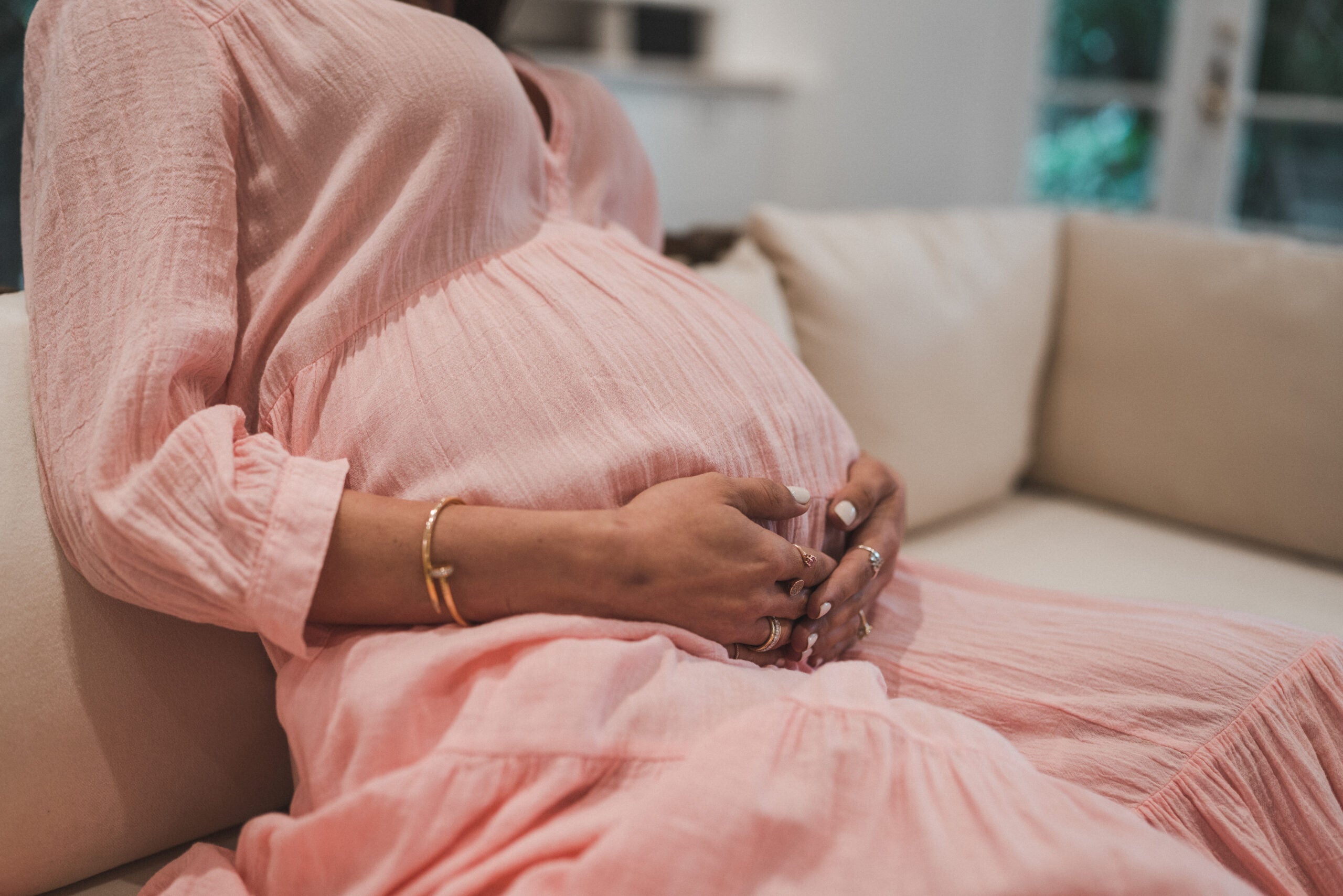 A pregnant woman in a pink dress is gently holding her pregnant belly - WeNatal Prenatal