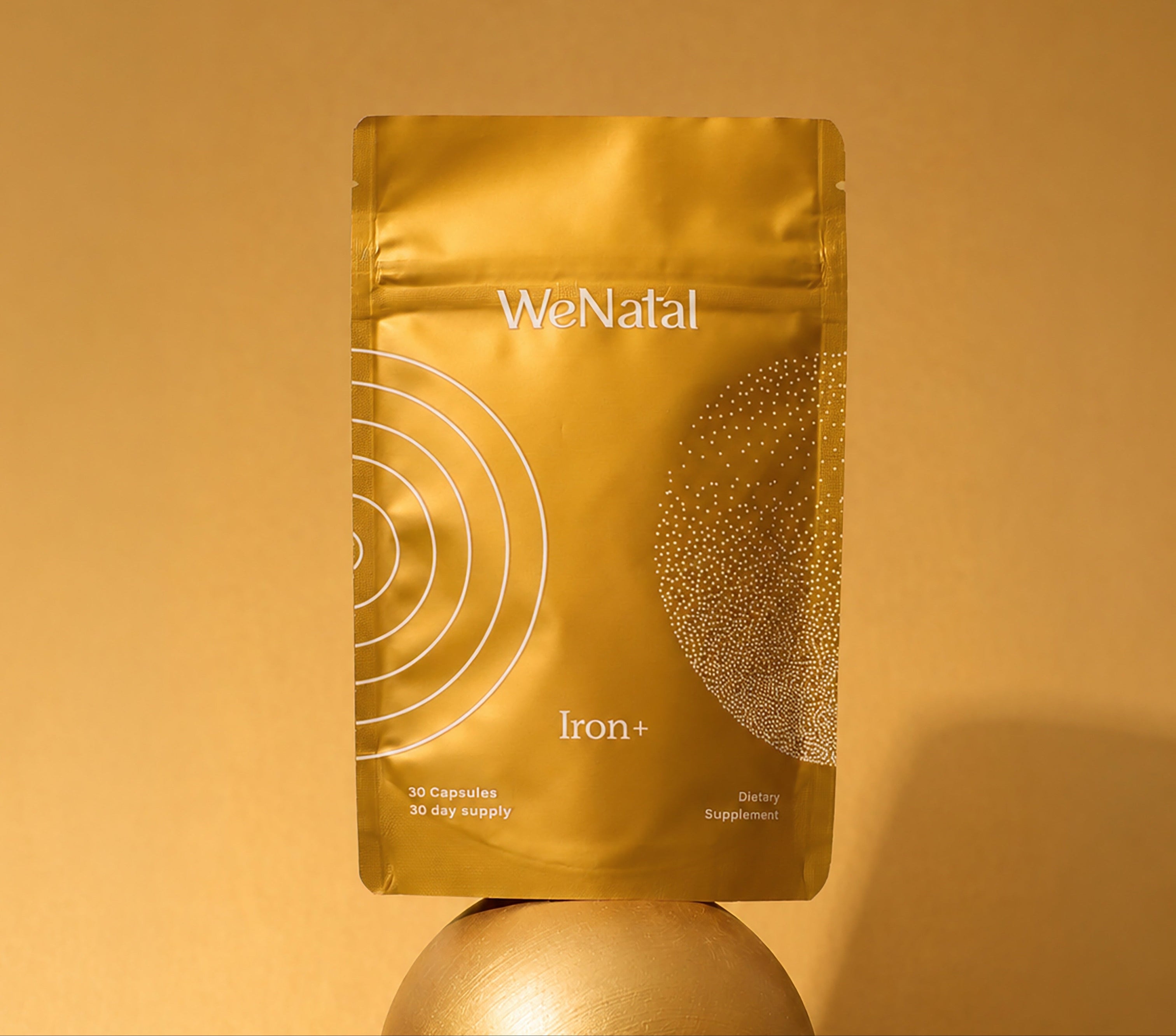 golden supplement pouch sitting on a golden ball - WeNatal Iron+
