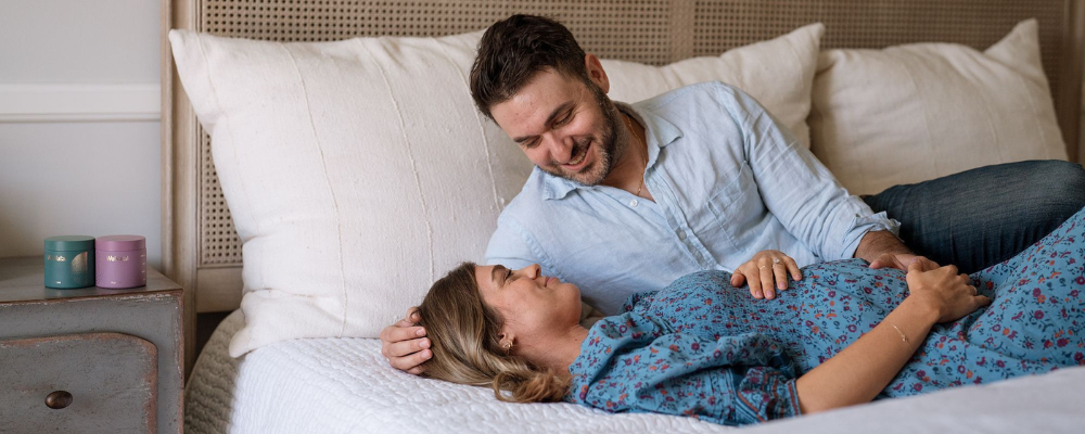 couple laying on bed holding smiling prenatal vitamins on night stand - Kosher prenatal vitamins for him and her - WeNatal prenatal vitamins