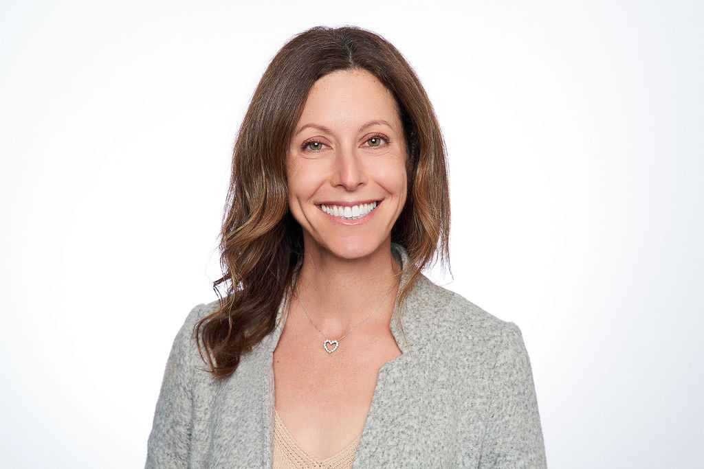 A woman smiling at the camera, wearing a necklace, possibly reflecting wellness and lifestyle elements associated with WeNatal's prenatal products.
