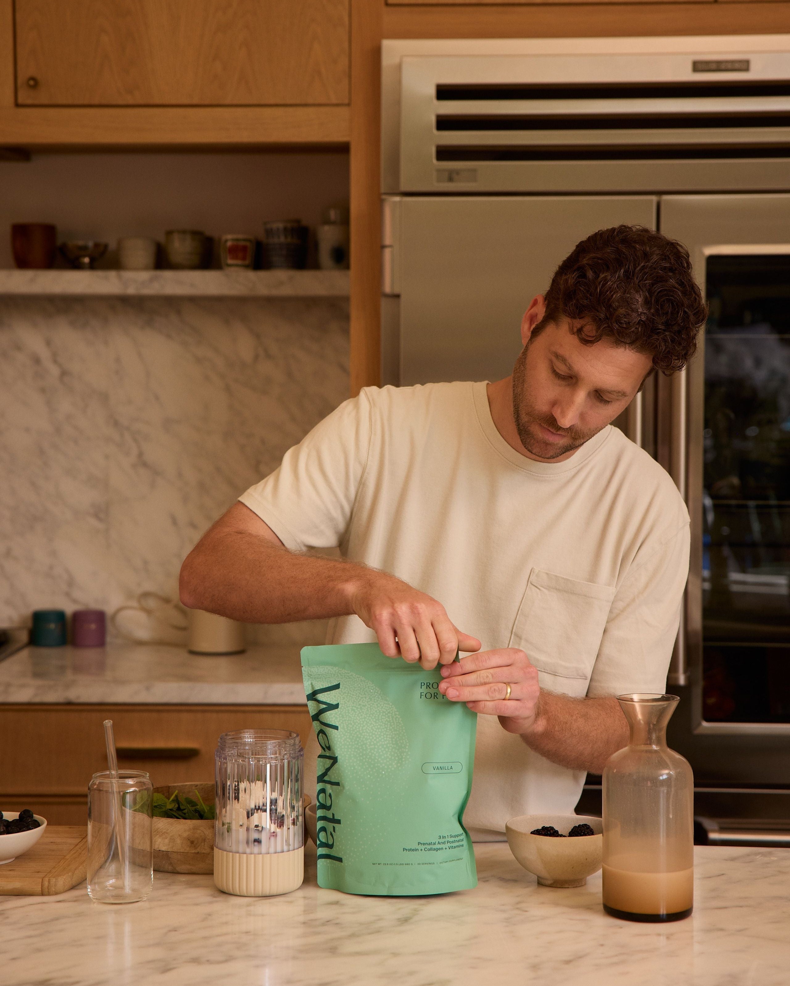 man in kitchen opening bag of fertility support protein powder - WeNatal Prenatal Protein+ for Him