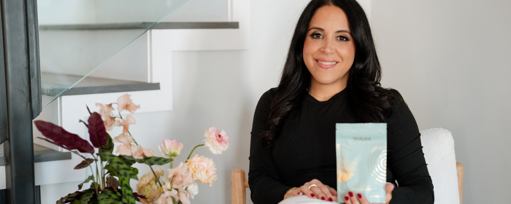 Vida holding a pouch of Magnesium Rest and Digest sitting next to a table with flowers - WeNatal Prenatal