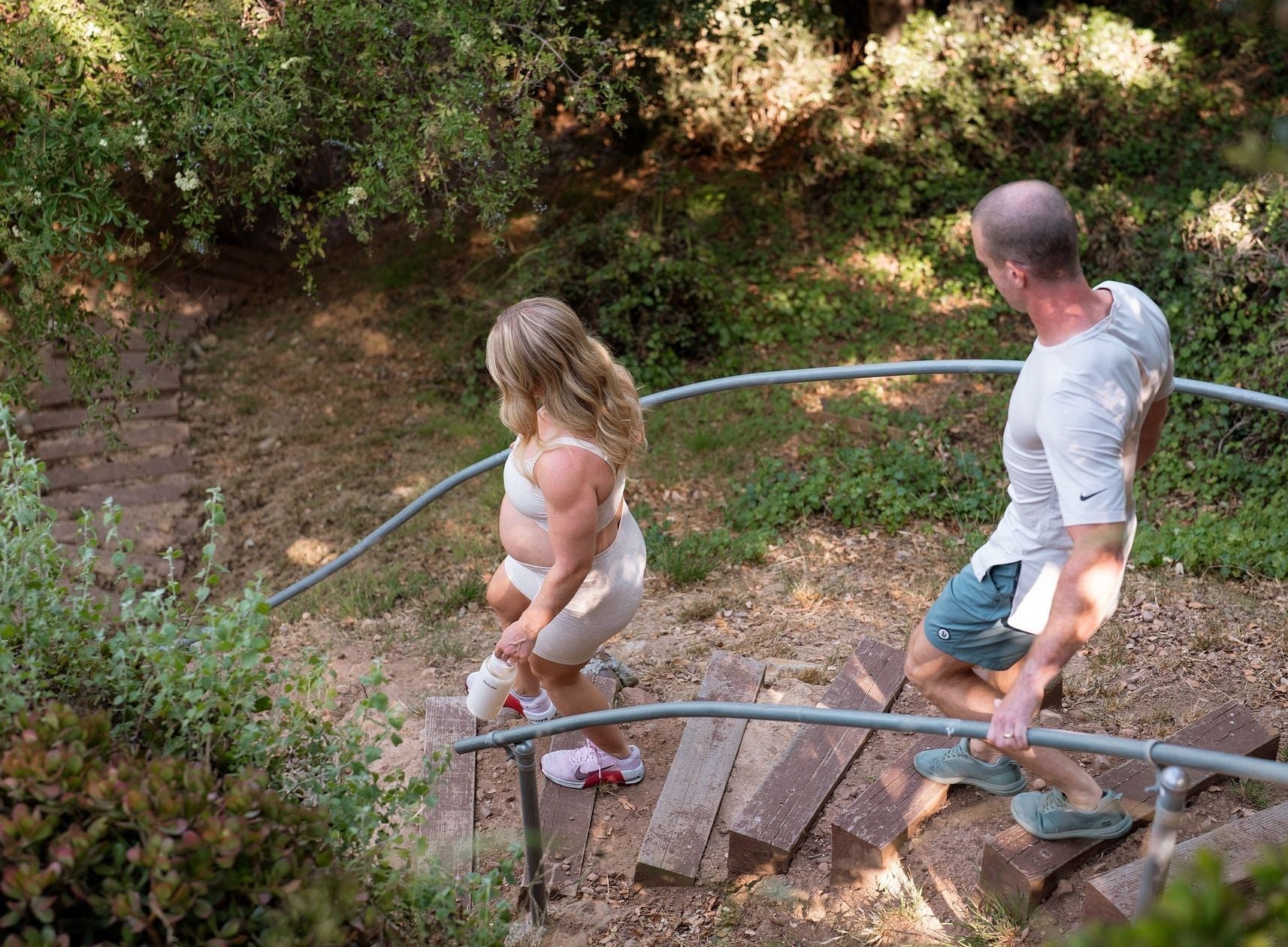 pregnant couple walking down stairs in forest area holding glass water bottles - Yoga for fertility - WeNatal prenatals for Her and Him