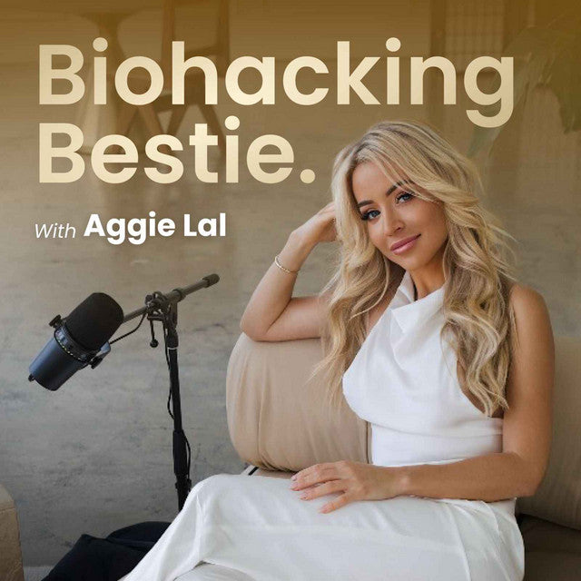 A woman in a white dress sits on a couch, smiling, with a microphone nearby, embodying relaxed elegance and wellness