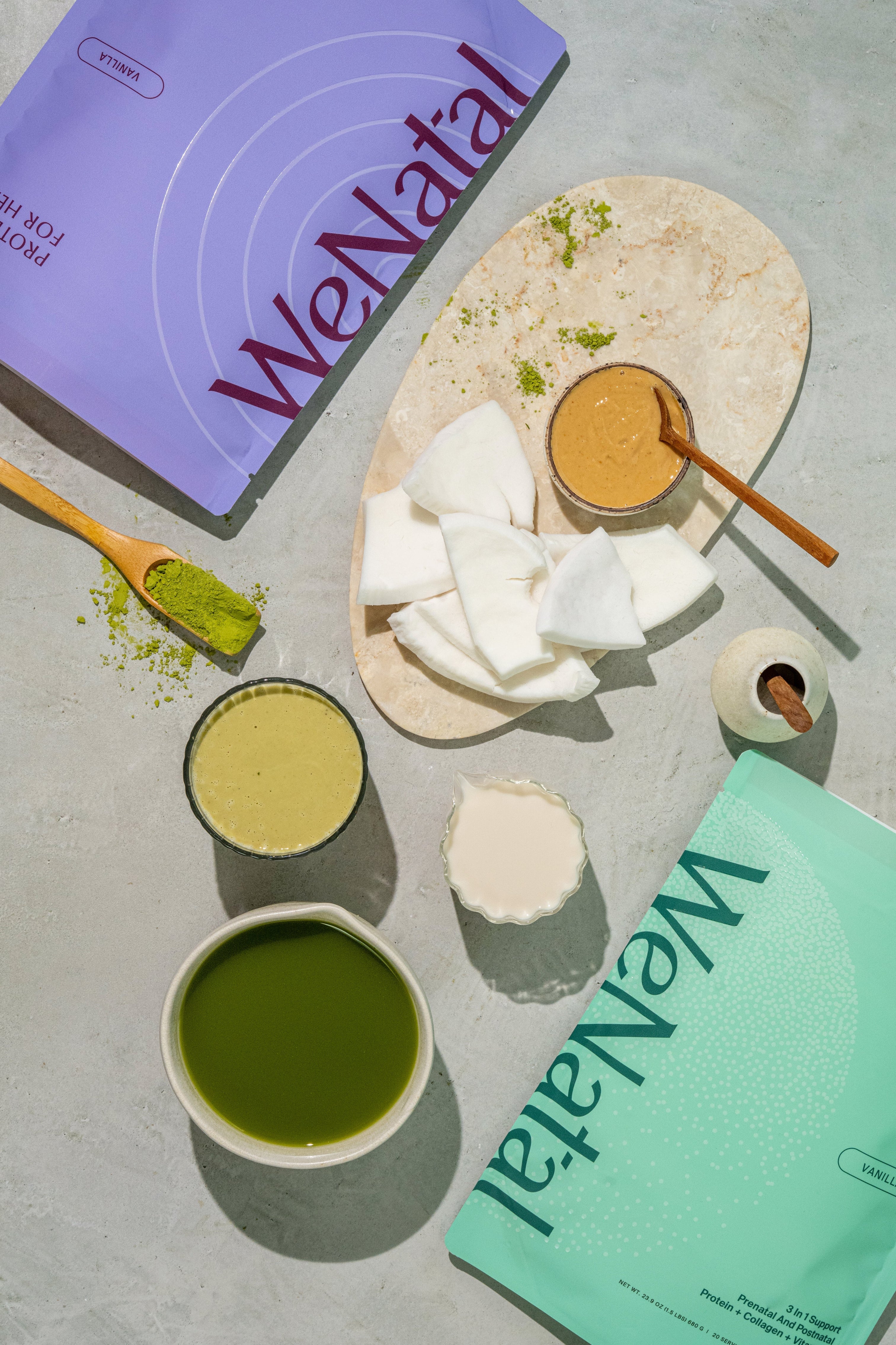 Prenatal Protein+ for Her and Prenatal Protein+ for Him bags laying on table top next to matcha green smoothie ingredients - WeNatal