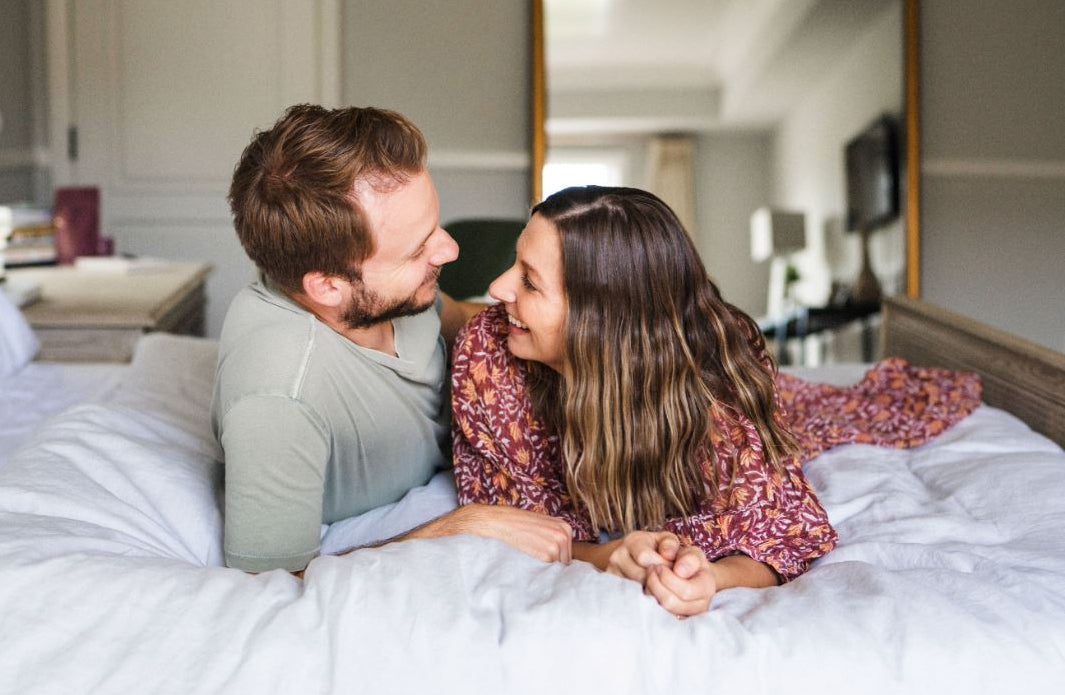 couple laying on bed looking at each other smiling - WeNatal prenatal - WeNatal male fertility supplement