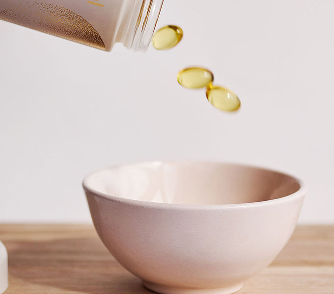 WeNatal Omega DHA+ Welcome Kit: Yellow-gold capsules spill from a container into a bowl, highlighting a prenatal supplement for daily nutrient and fertility support