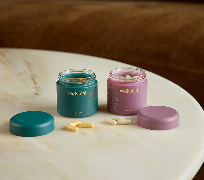 WeNatal Together Welcome Kit featuring prenatal supplements: teal jar For Him with yellow capsules and mauve jar For Her with off-white capsules, offering daily nutrient and fertility support.