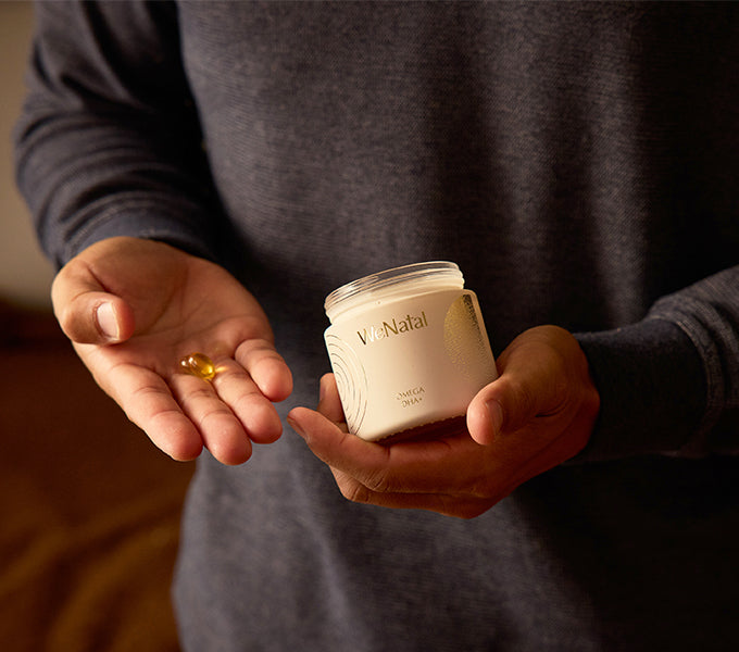 Person holding WeNatal Omega DHA+ Welcome Kit, showcasing two soft-gel capsules; a prenatal supplement offering daily nutrient and fertility support with omega-3 DHA for prenatal nutrition.