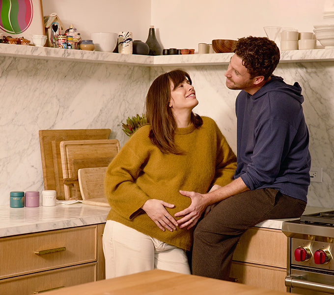 Couple in a kitchen sharing a tender moment, highlighting WeNatal Together Welcome Kit—prenatal supplement capsules for Him + Her, supporting daily nutrient and fertility needs.