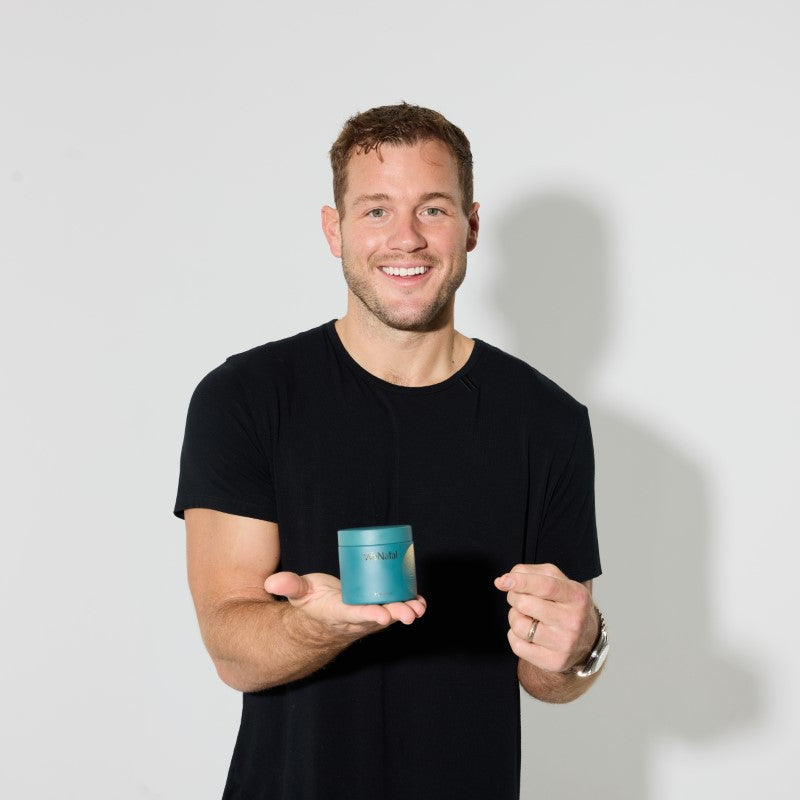 A man wearing a black shirt holding a WeNatal For Him glass jar on his palm and pointing at it using his other hand