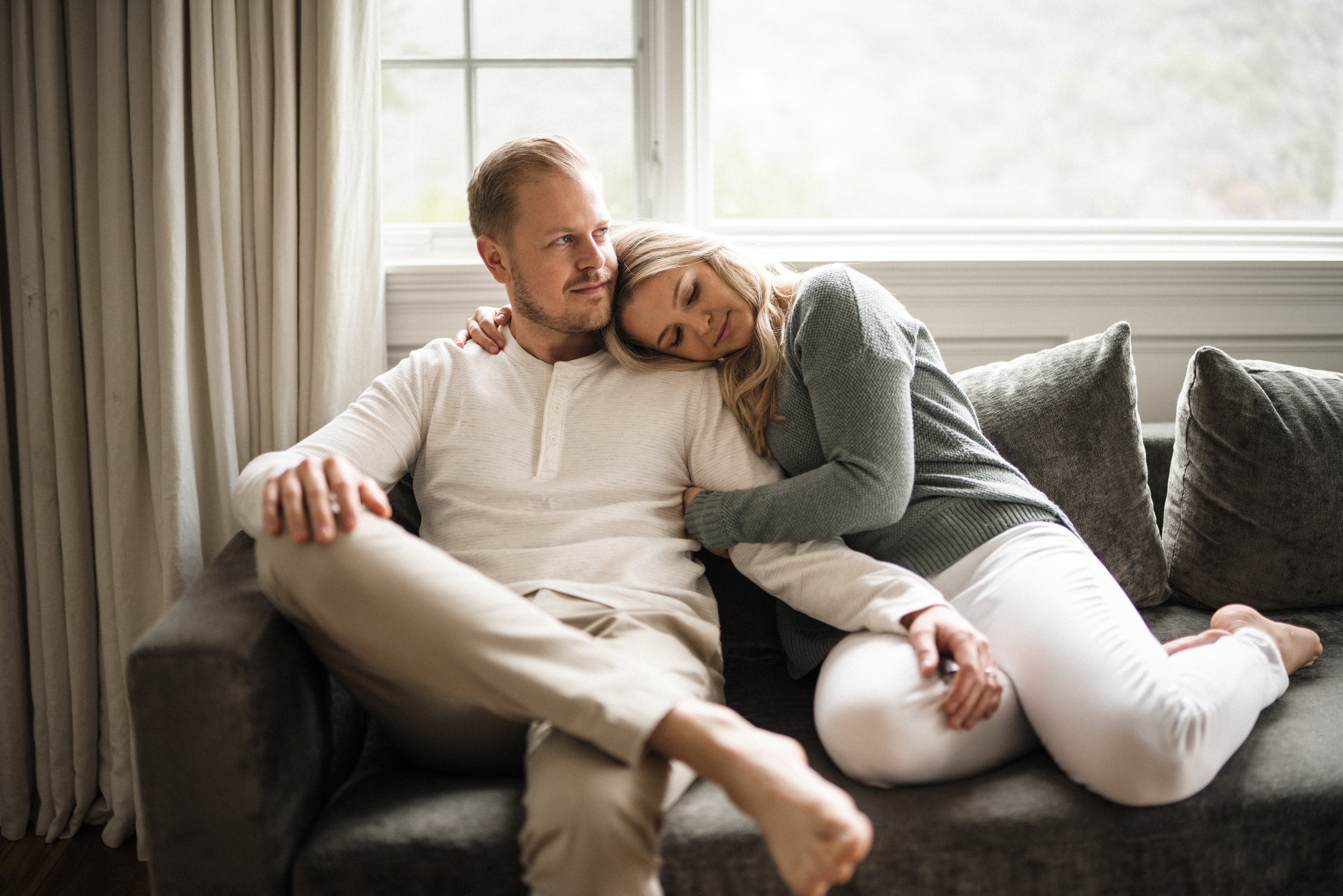 Image of a blonde haired man and blonde haired woman couple cuddling on a grey couch