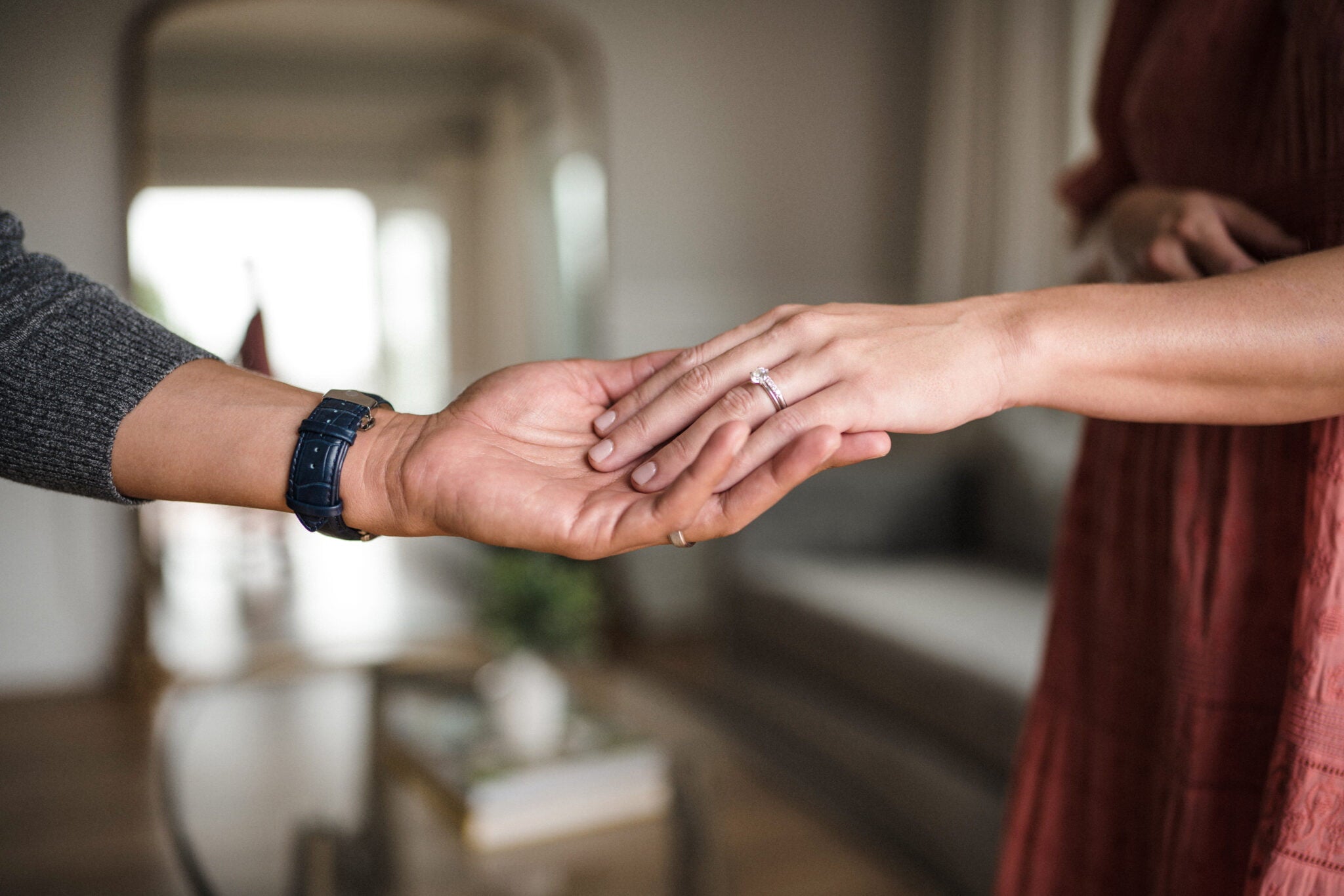 photo of a girl's hand wearing a diamond ring on top of a guys's hand wearing a watch and a wedding ring
