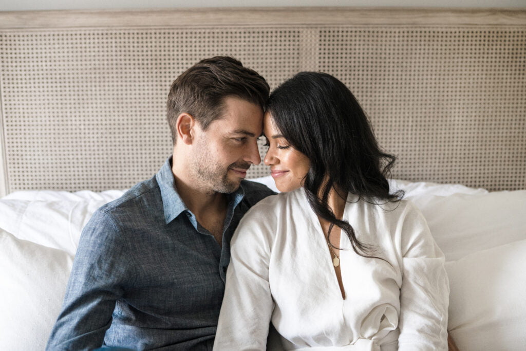 photo of a smiling couple sitting on bed with nose to nose pose