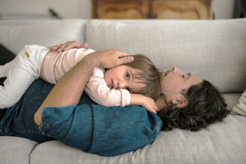 photo of a dad lying on a couch while he has his child lying on his chest