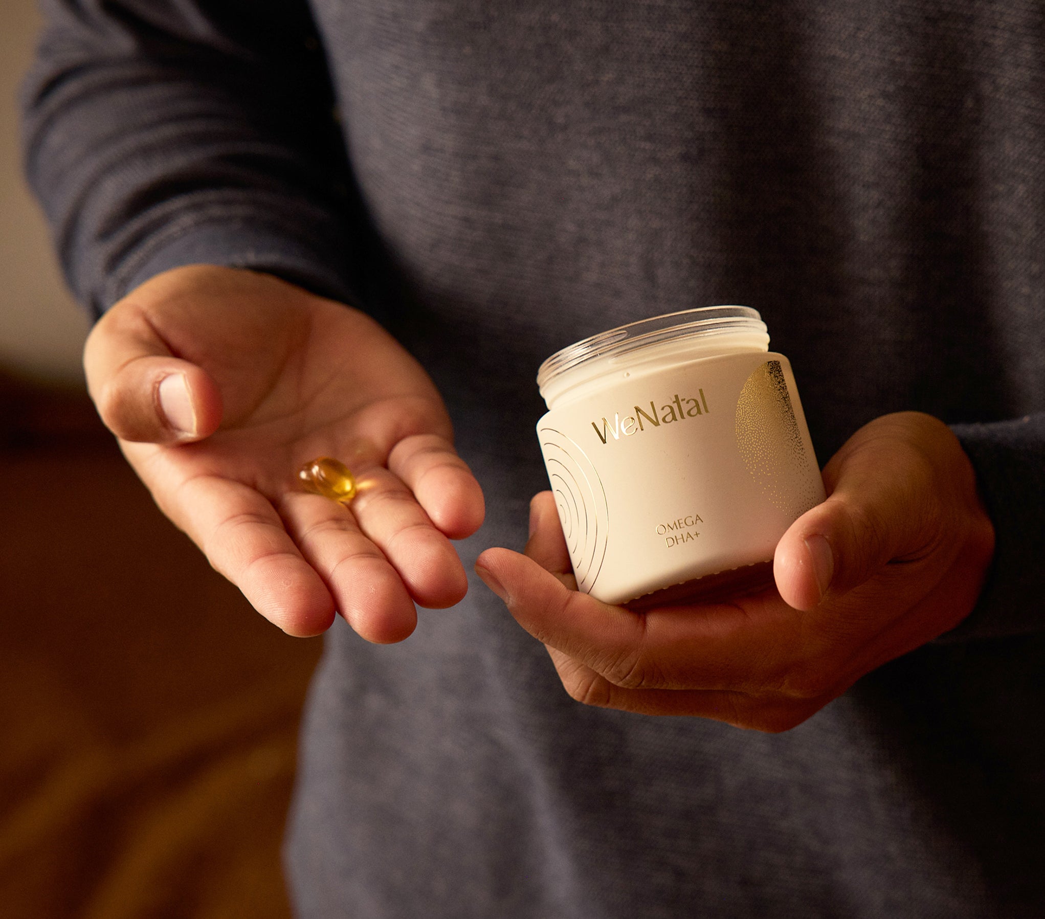 Person holding Omega Together Welcome Kit - NEW, showcasing WeNatal Omega DHA+ prenatal supplements, including jar and two omega-3 DHA softgel capsules for daily nutrient support