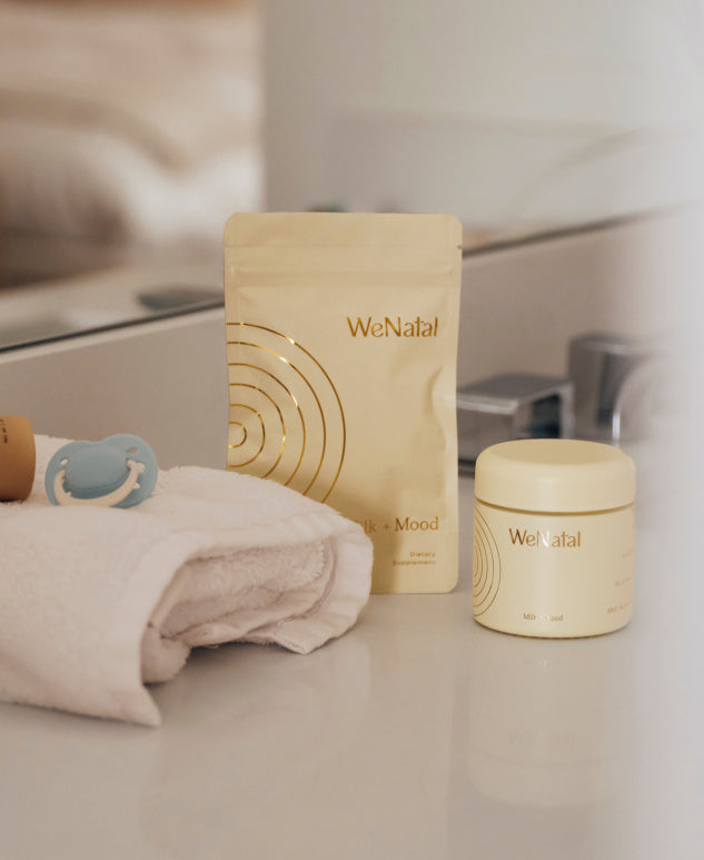 WeNatal Milk + Mood pouch and jar on a nursery counter next to a folded towel and pacifier