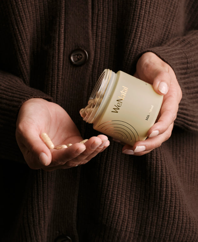 Hands pouring capsules from a WeNatal Milk + Mood jar