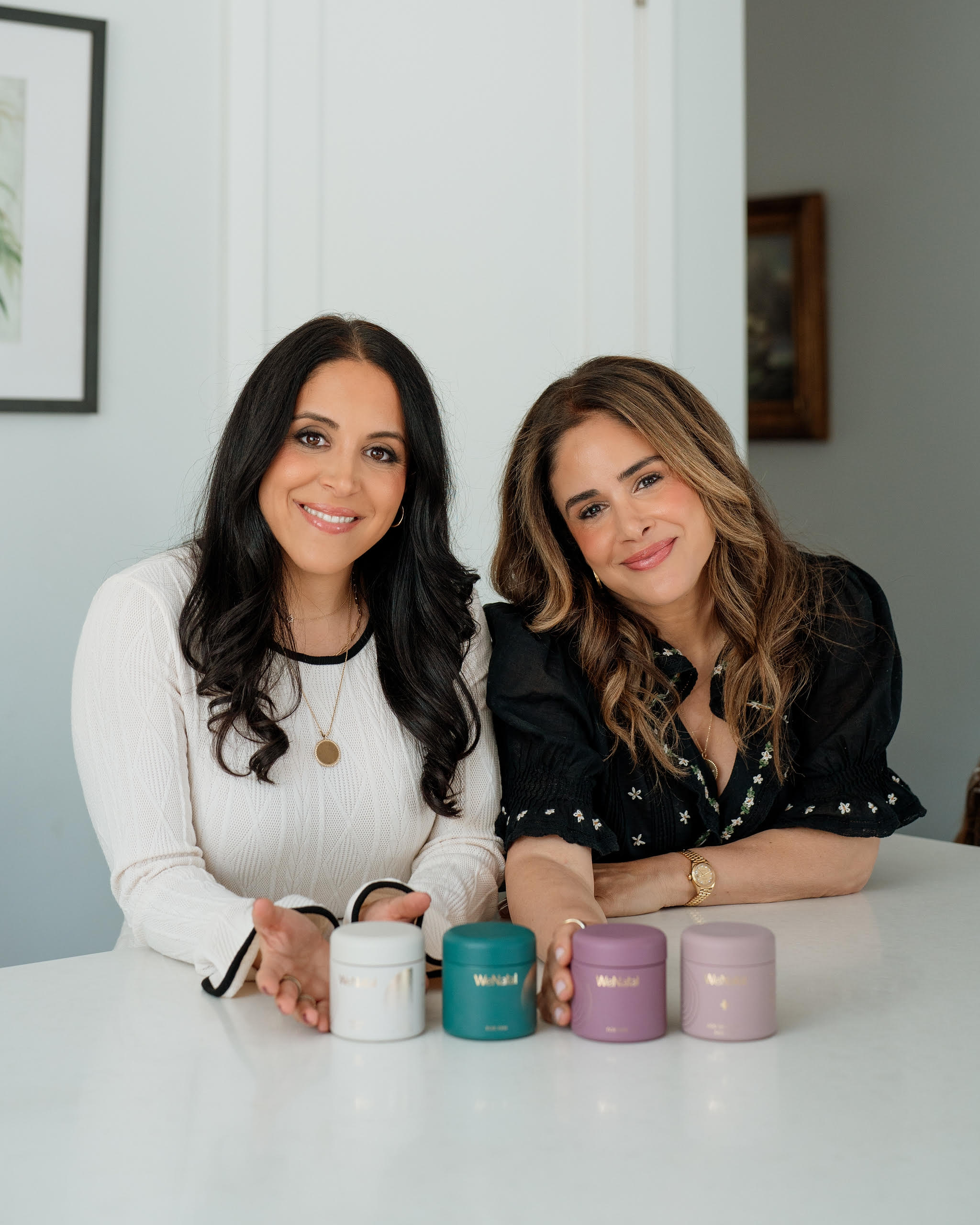 Two women sitting at a table with small containers in front of them