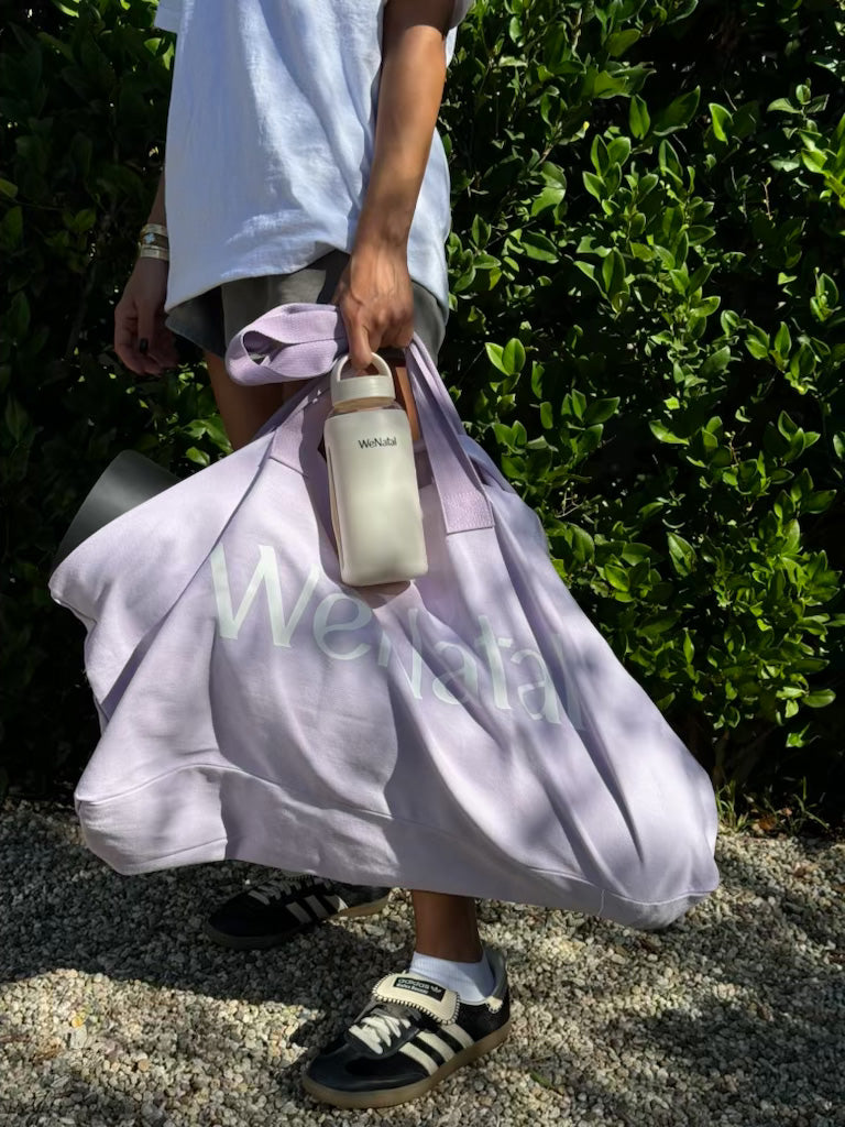 Person holding the Free Everything Tote and a bottle, showcasing its spacious design and versatility for carrying various essentials.