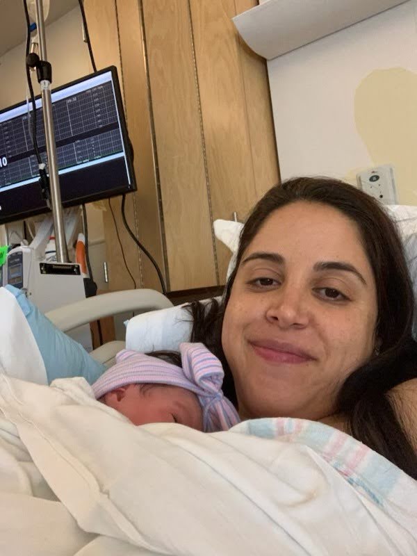 A new mother smiling for a photo with her newborn in a hospital room