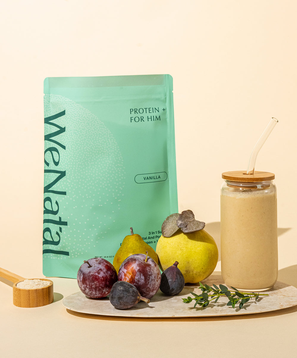 WeNatal Protein+ For Him vanilla powder in a teal pouch, wooden scoop, and a smoothie jar, styled with fresh fruit for prenatal nutrient support