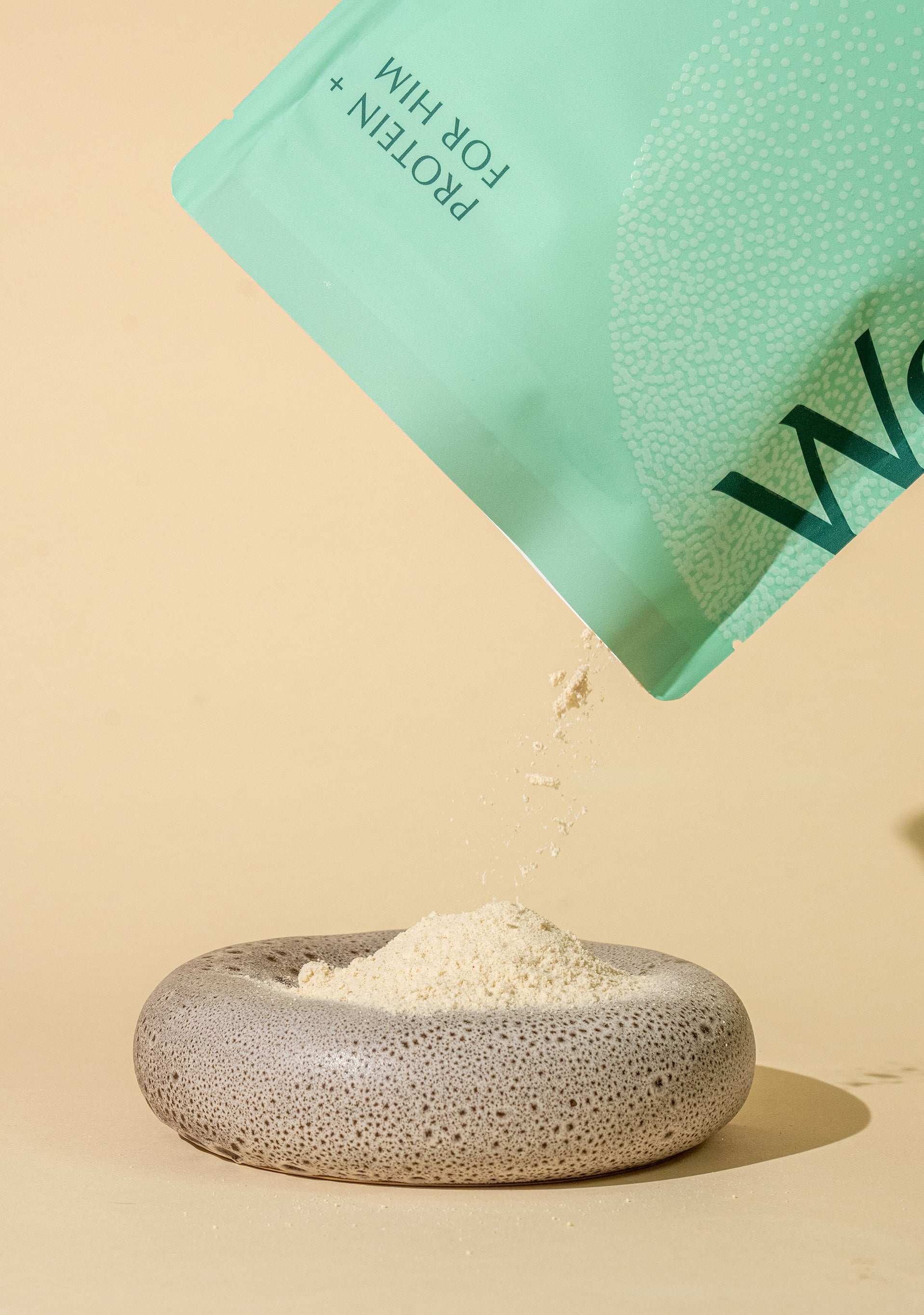 WeNatal Protein + for Him pouch pouring fine powder into a stone dish, showcasing the supplement's presentation and packaging design