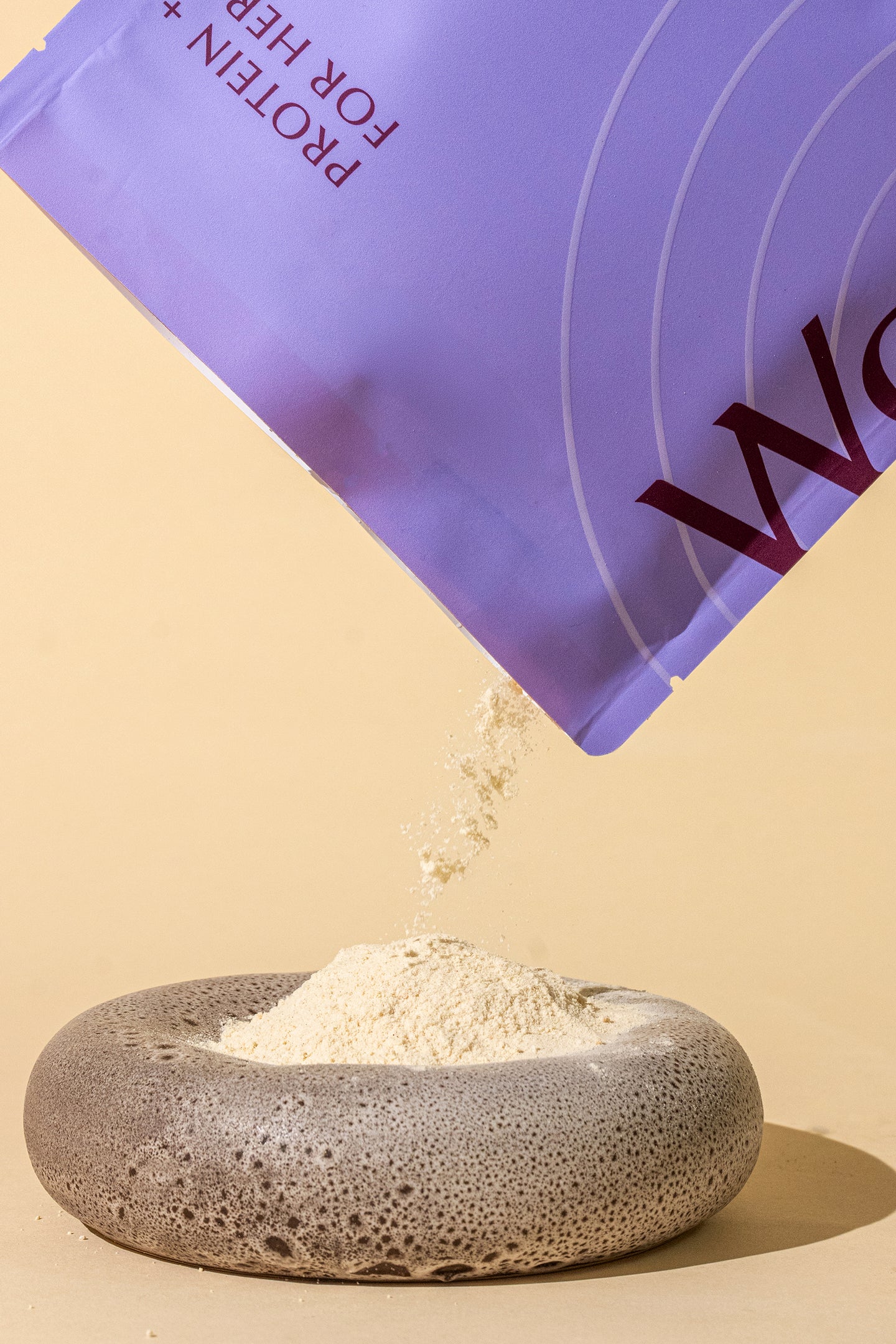 WeNatal Protein + for Her pouch pouring beige protein supplement powder into a rounded stone dish, emphasizing nutrition for women's health.