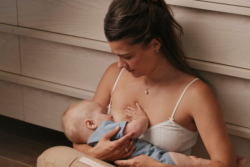 Mother breastfeeding her baby on a nursing pillow while sitting on the floor, with a jar of WeNatal Milk + Mood nearby - WeNatal Milk + Mood