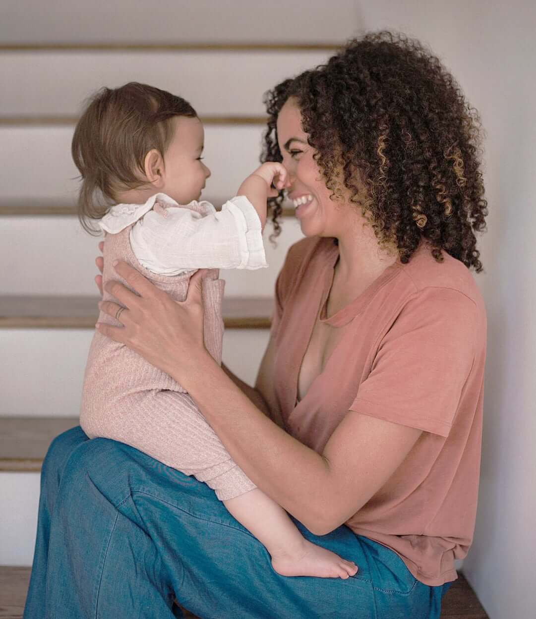 a mom playing with her baby on her lap while she is sitting in the stairs